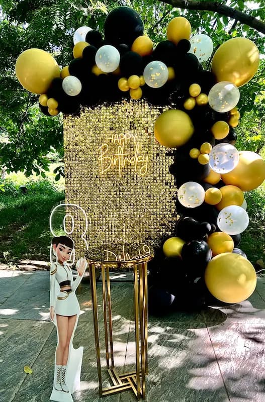 دکور تولد تم K-Pop با بکگراند طلایی اکولایزر، بادکنک مشکی و طلایی، نوشته Happy Birthday نئون و استند کاراکتر دختر K-Pop"