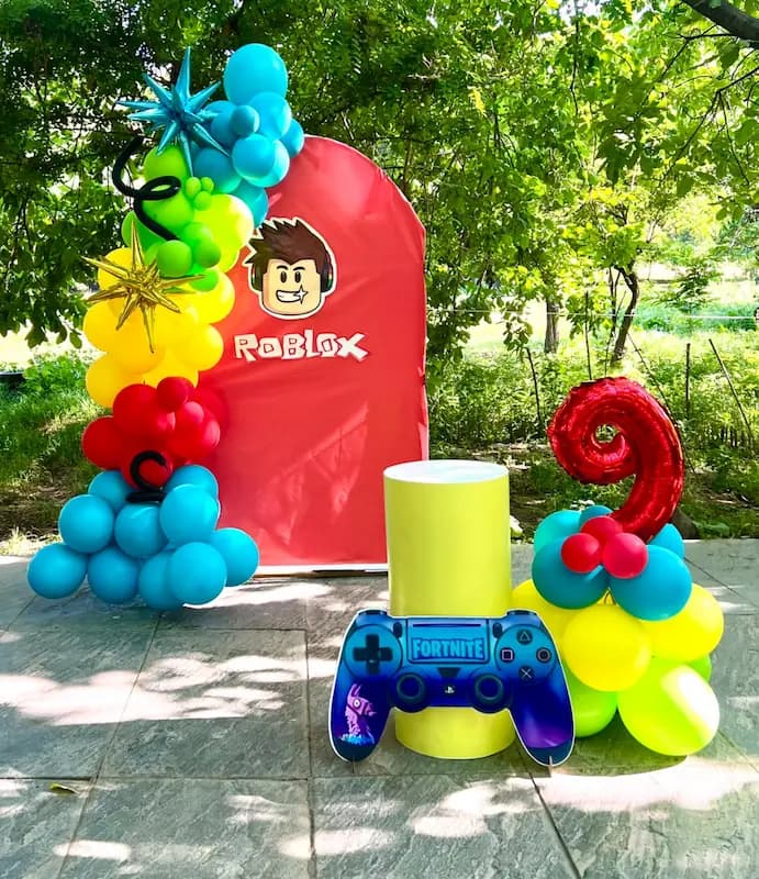 alt="دکور تولد با تم Roblox با بادکنک رنگارنگ، بکگراند قرمز Roblox، کنترلر و عدد ۲"