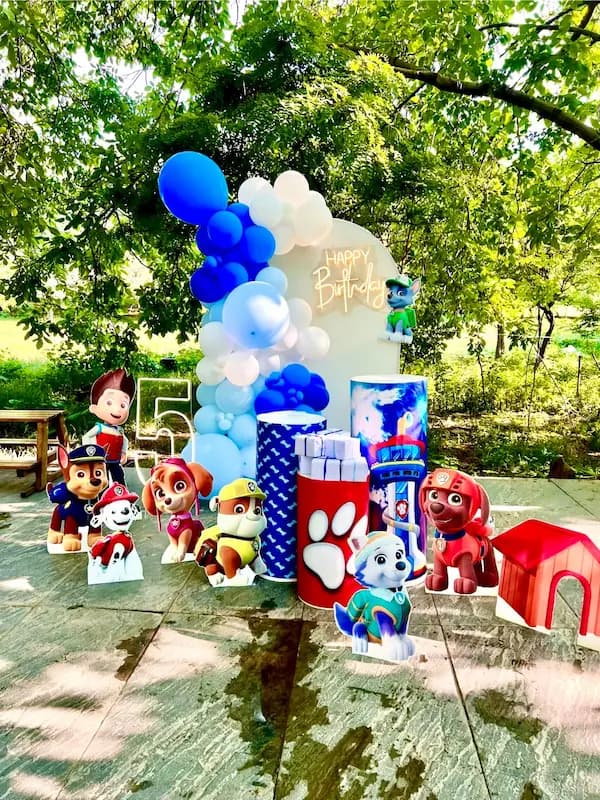 دکور تولد با تم Paw Patrol با استندهای شخصیتهای chase، Marshall، Skye، Rubble، Rocky و Everest، بادکنک آبی و سفید، عدد ۵ و خانه سگ"