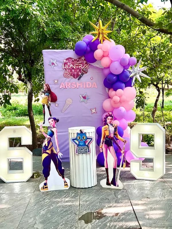 "دکوراسیون تم تولد K-Pop Demon Hunters با بادکنک بنفش و صورتی، بکگراند یاسی و استند کاراکترها"